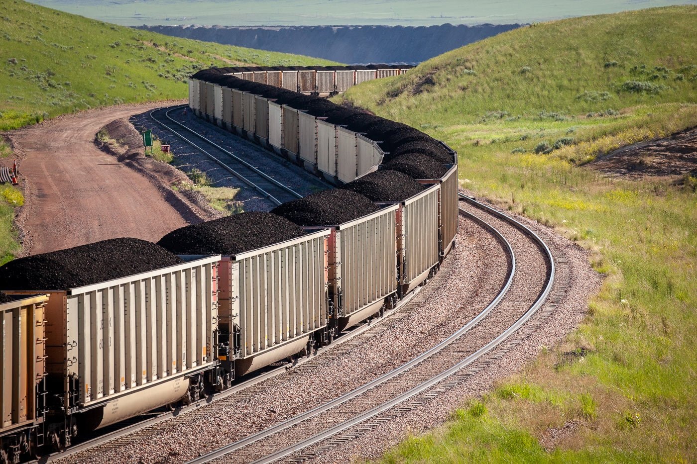 Coal rail cars curving through rolling Wyoming hills near the Powder River Basin